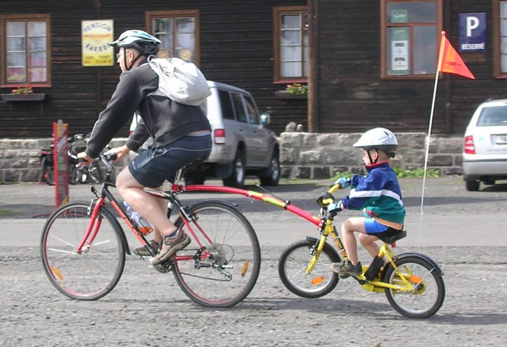 Man on bicycle with small child's bike attached as trailer