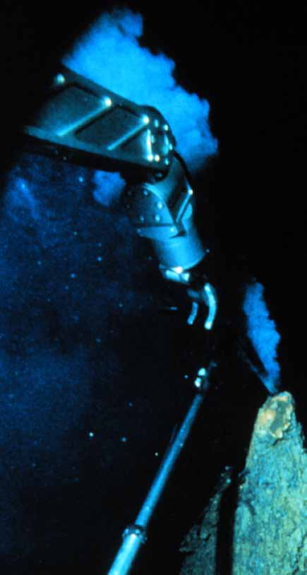 Black chimney smoker seen through the view port of the Alvin sub at a deep sea vent, deep under the Pacific Ocean. The metal claw is a manipulator arm from the submarine.  